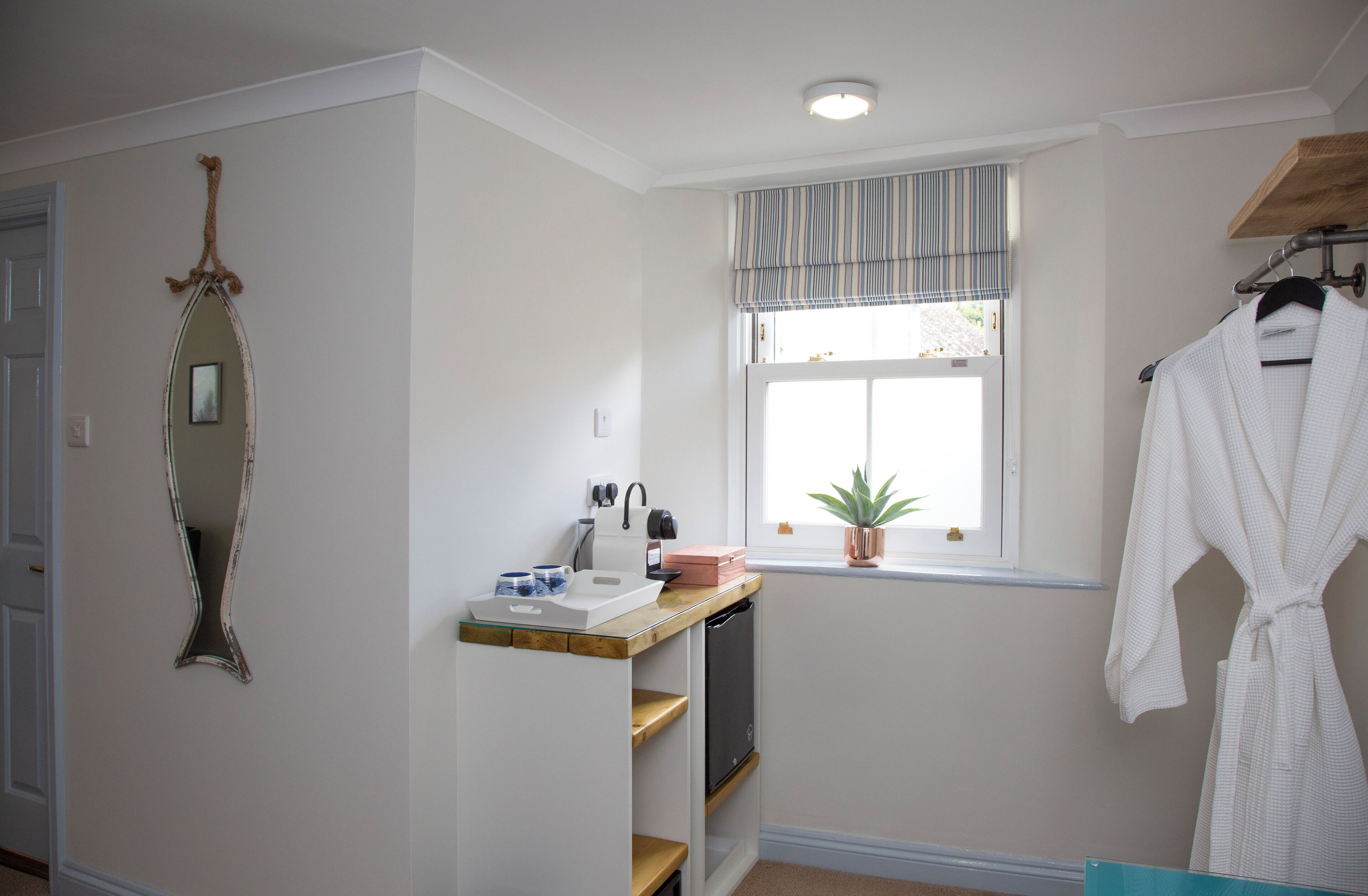 A bathroom with a vanity, a mirror, a window with a plant, and a robe hanging on a rack.