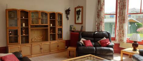 A living room with a leather sofa, a glass-top coffee table, a wooden cabinet with glass doors, and a black leather armchair.