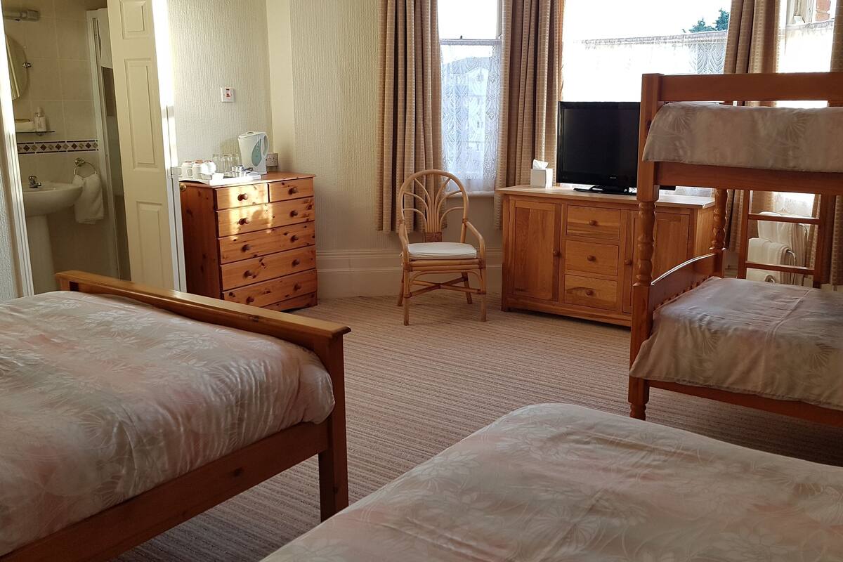 Een slaapkamer met twee houten stapelbedden, een houten dressoir, een stoel, een televisie en een badkamer die door een open deur zichtbaar is.