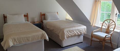 A bedroom with two beds, a chair, a nightstand, and a painting on the wall.