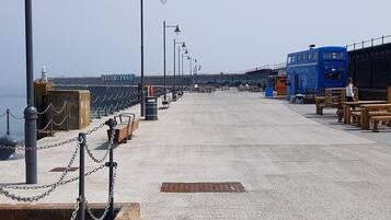 A seaside promenade with a blue bus, benches, and a sign reading "FOLKEISSTONE".
