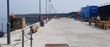 A seaside promenade with a blue bus, benches, and a sign reading "FOLKEISSTONE".