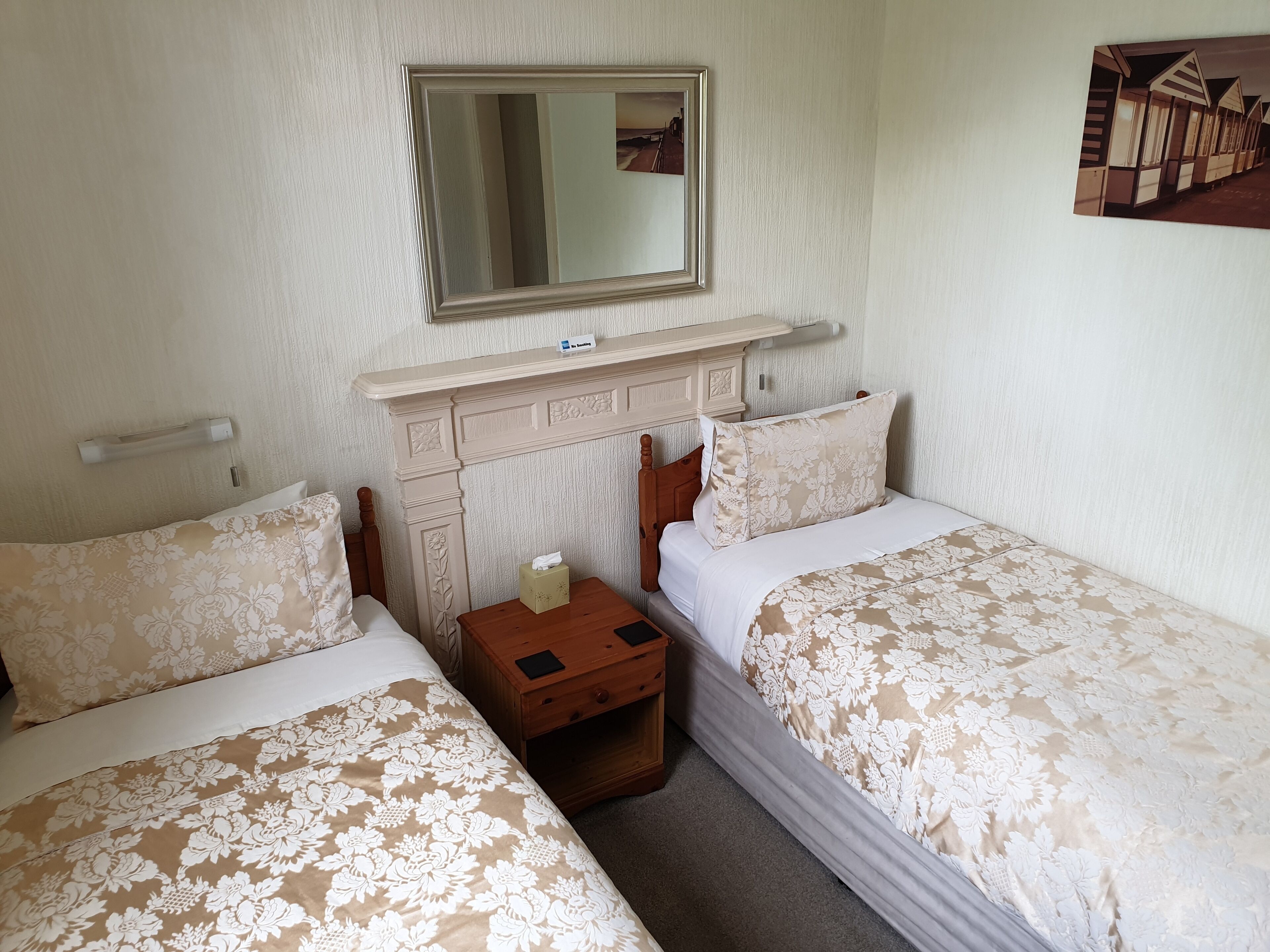 Un dormitorio con dos camas, una mesita de noche, un espejo y un estante en la pared.