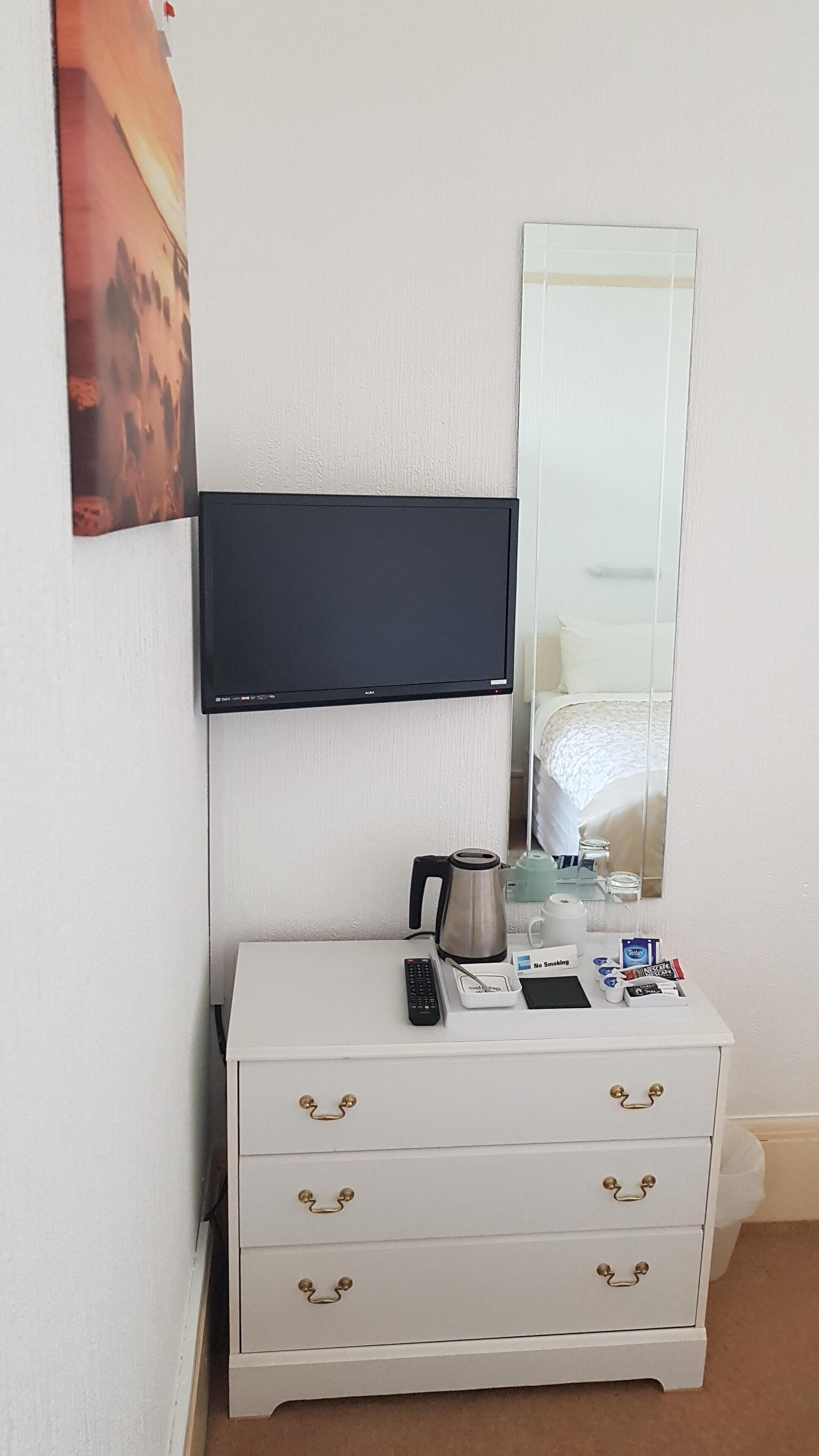 A hotel room with a white dresser, a flat-screen TV, a coffee maker, a remote control, and a "No Smoking" sign.