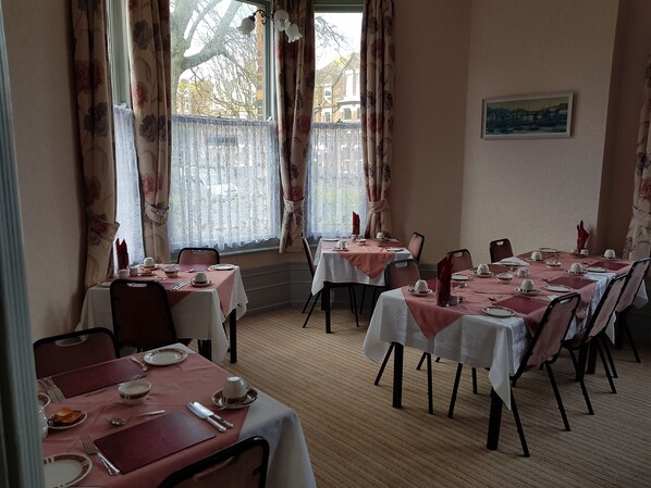 Comedor con mesas dispuestas para comidas, cortinas con motivos florales y vistas a edificios.