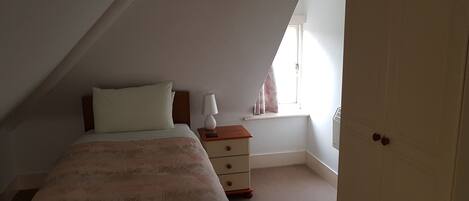A bedroom with a bed, a nightstand, a lamp, a window with curtains, and a door.