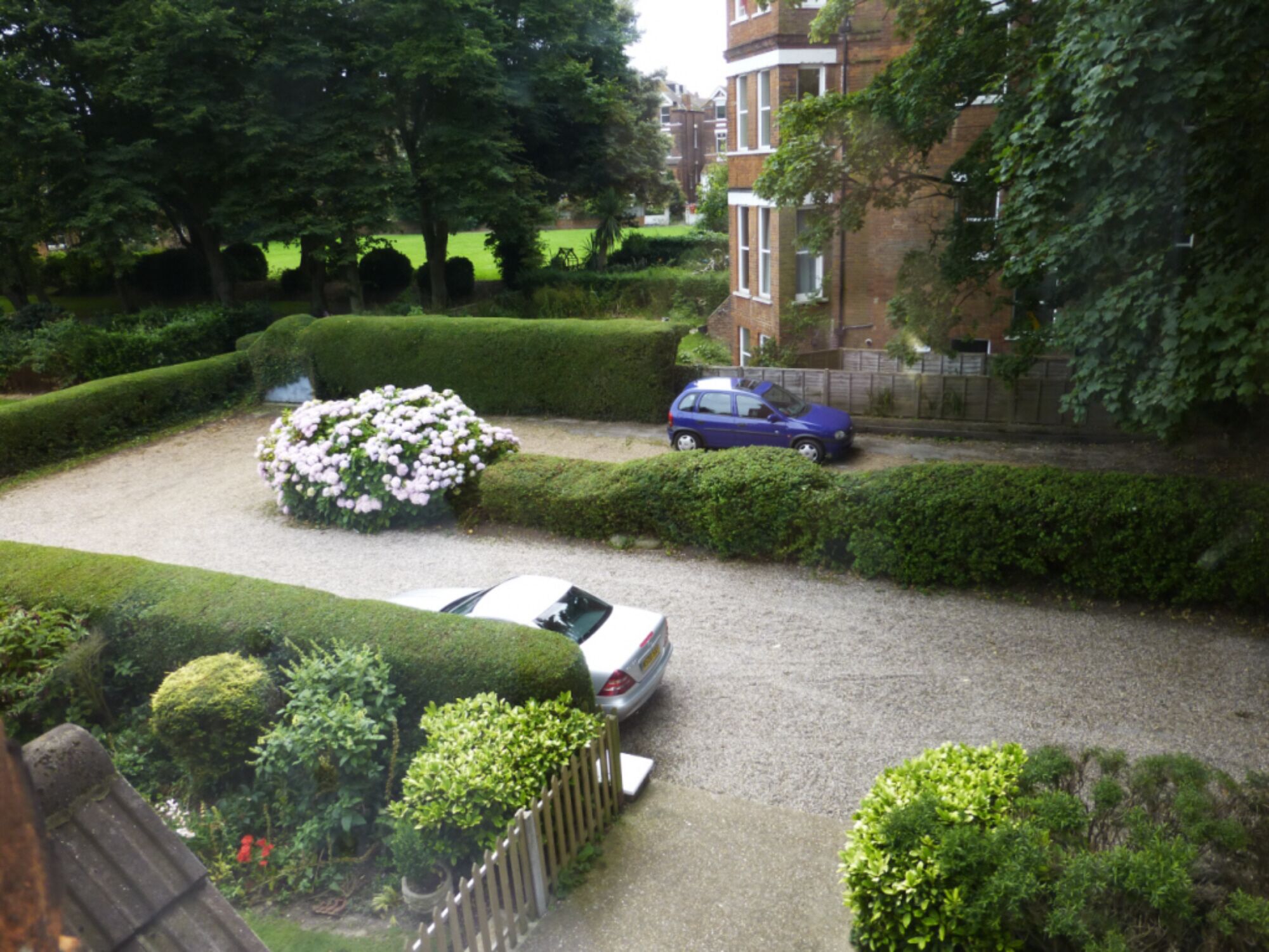 A residential area with a gravel driveway, neatly trimmed hedges, and a parked car.