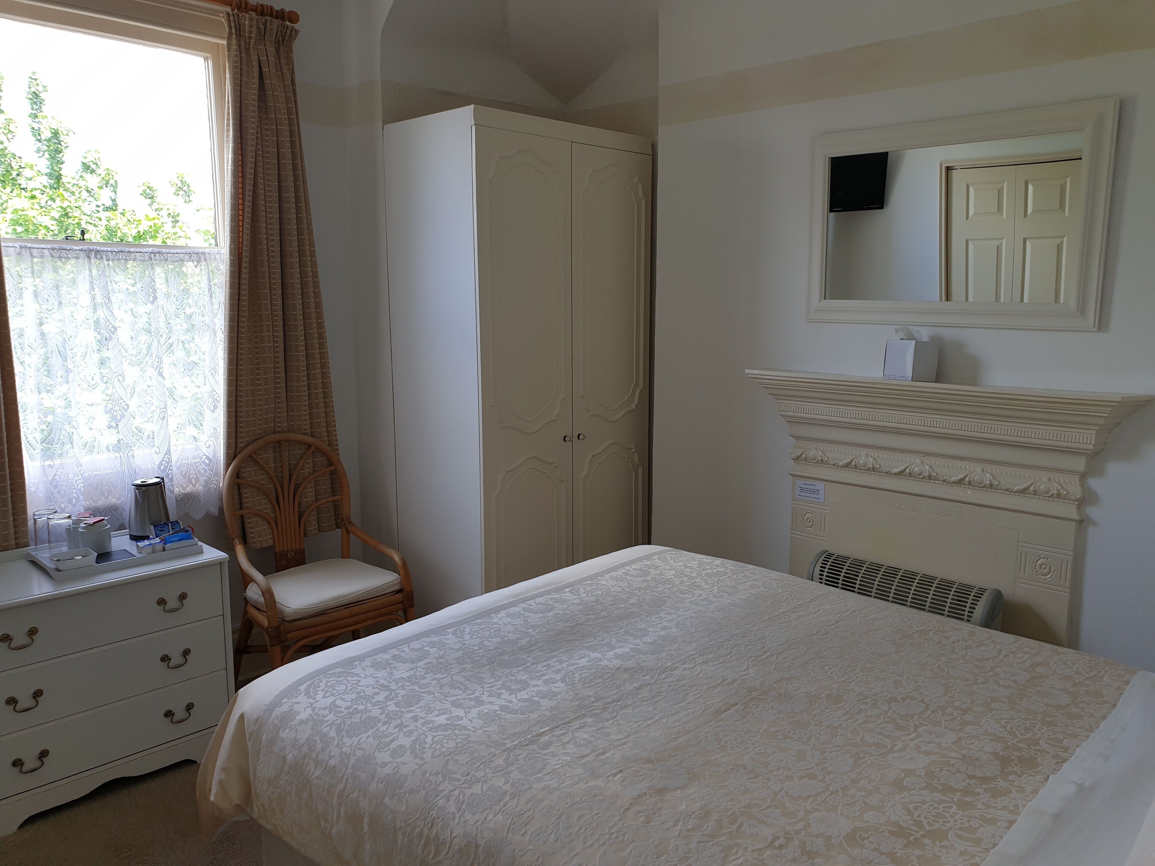 A bedroom with a bed, a wardrobe, a chair, a dresser, a mirror, and a fireplace.