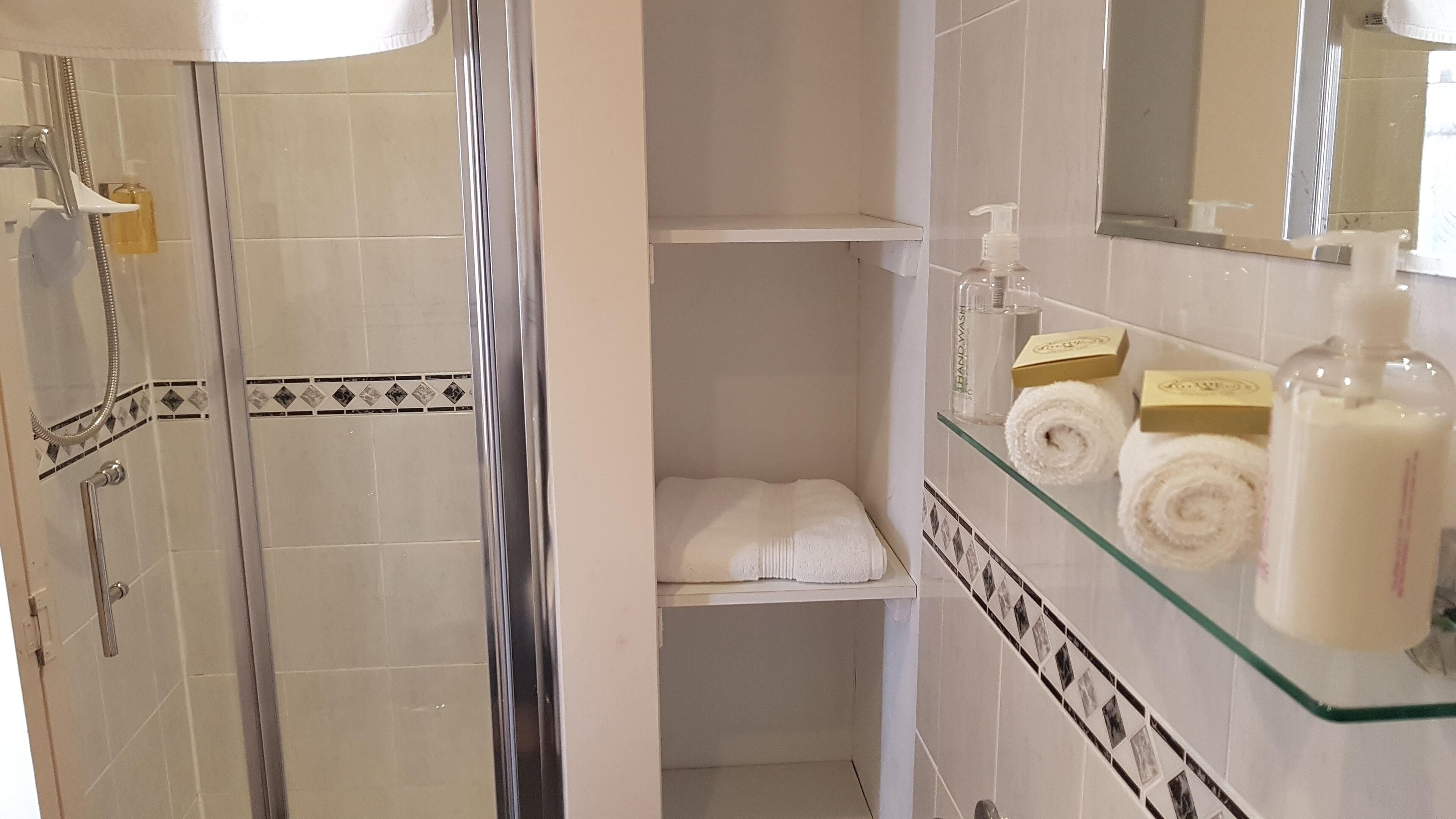 Casa de banho com cabine de duche em vidro, prateleira de vidro com artigos de higiene e toalheiro.