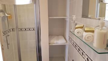Casa de banho com cabine de duche em vidro, prateleira de vidro com artigos de higiene e toalheiro.