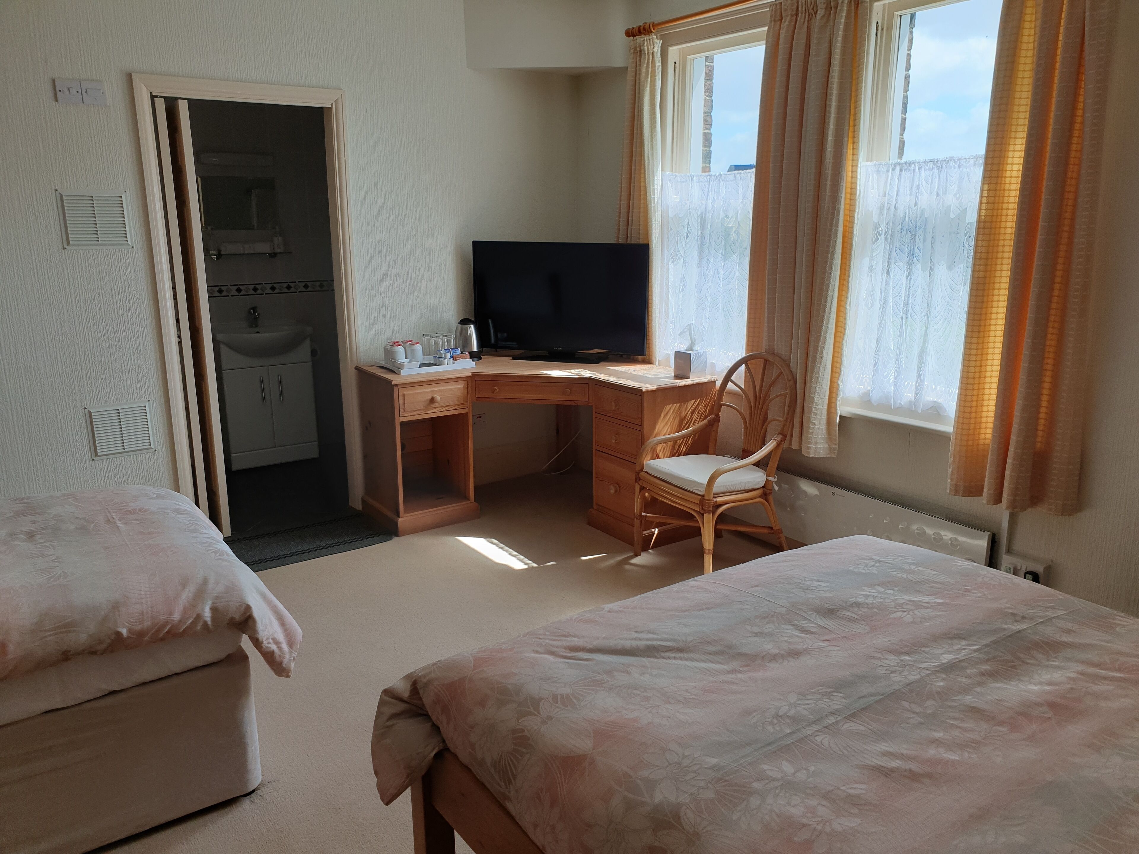 A hotel room with a bed, a desk with a chair, a television, and a window with curtains.