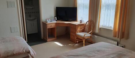 A hotel room with a bed, a desk with a chair, a television, and a window with curtains.