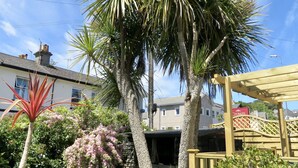 A garden with palm trees, a wooden pergola, and a building in the background. - Bentley Lodge Guest House (Torquay)