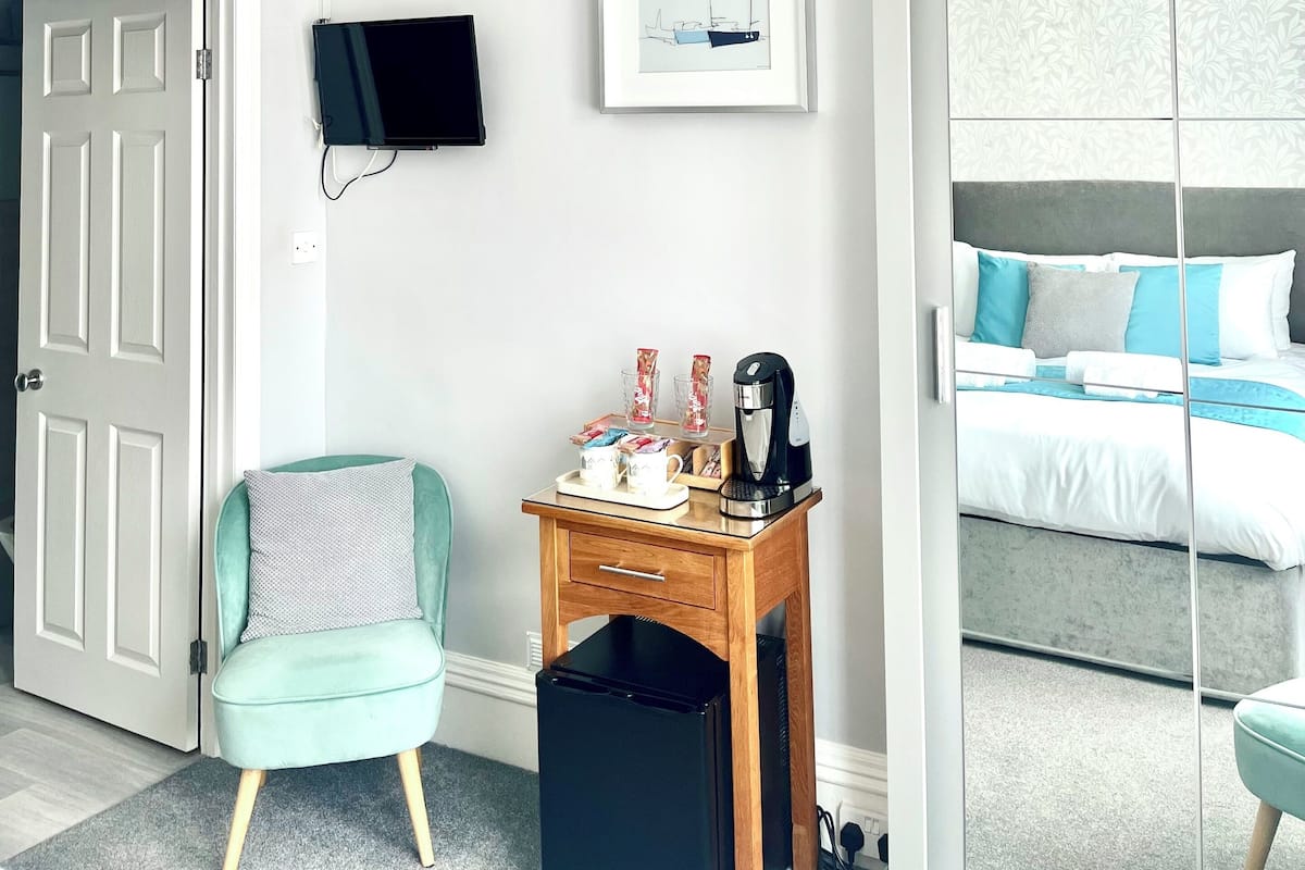 Une chambre d’hôtel avec un lit, un téléviseur fixé au mur, une petite table avec une machine à café et une chaise.
