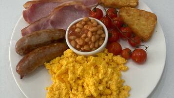 A plate of breakfast food including sausages, bacon, scrambled eggs, beans, tomatoes, and toast.