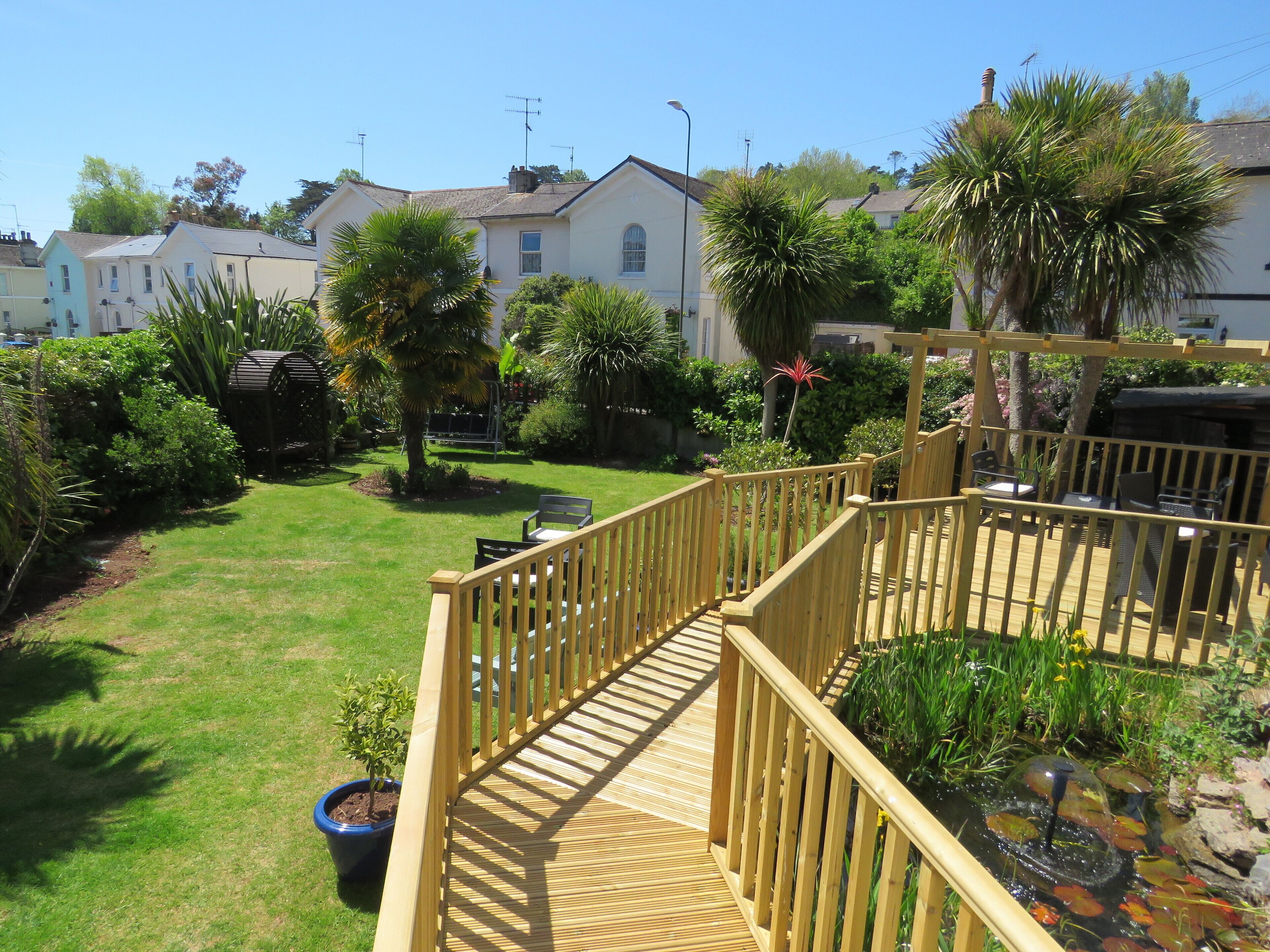 A wooden deck with a railing, surrounded by a well-maintained garden with various plants and a small pond.