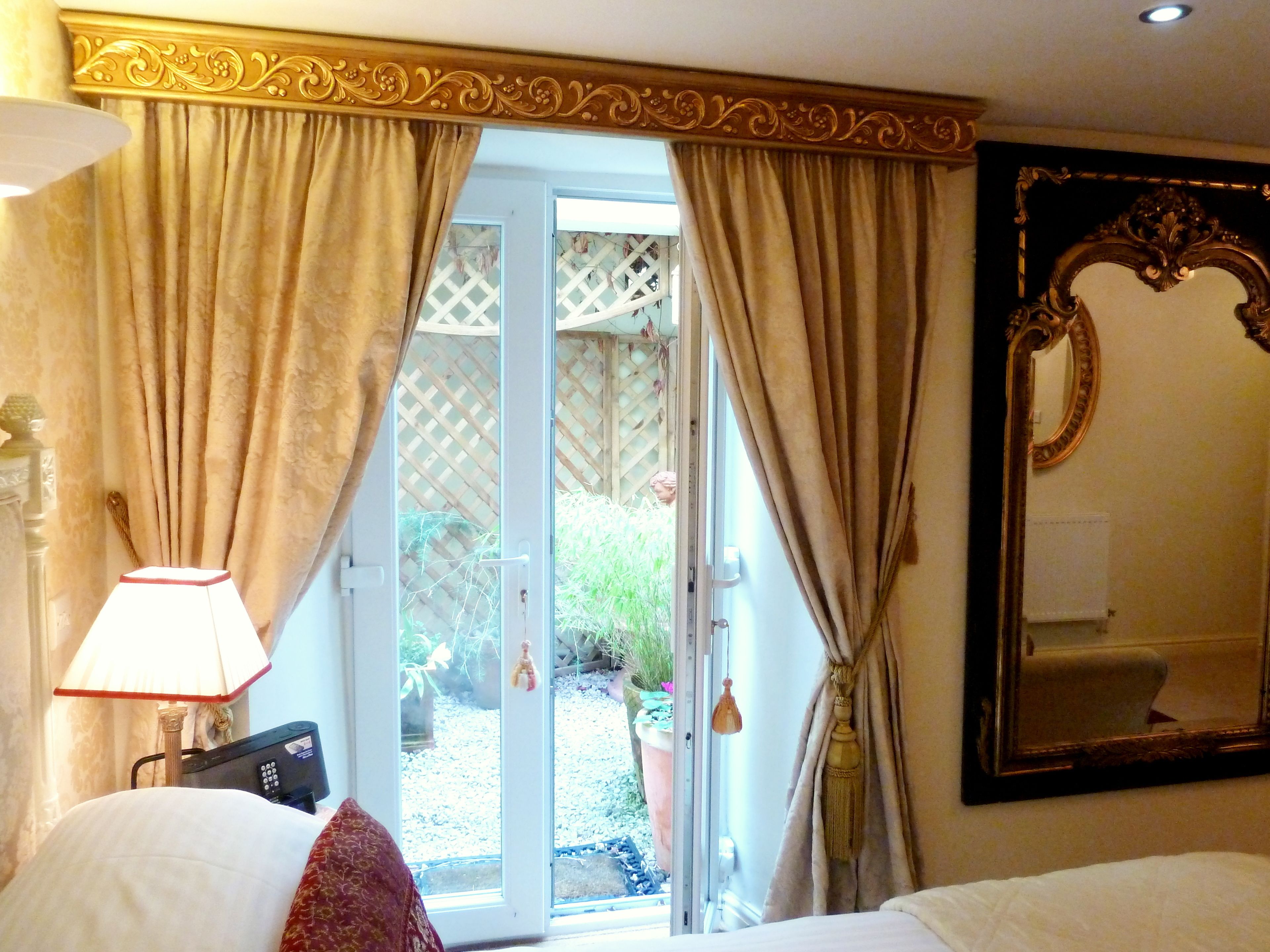 A hotel room with a bed, a lamp, a large mirror, and a sliding glass door leading to a garden.