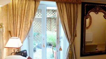 A hotel room with a bed, a lamp, a large mirror, and a sliding glass door leading to a garden.