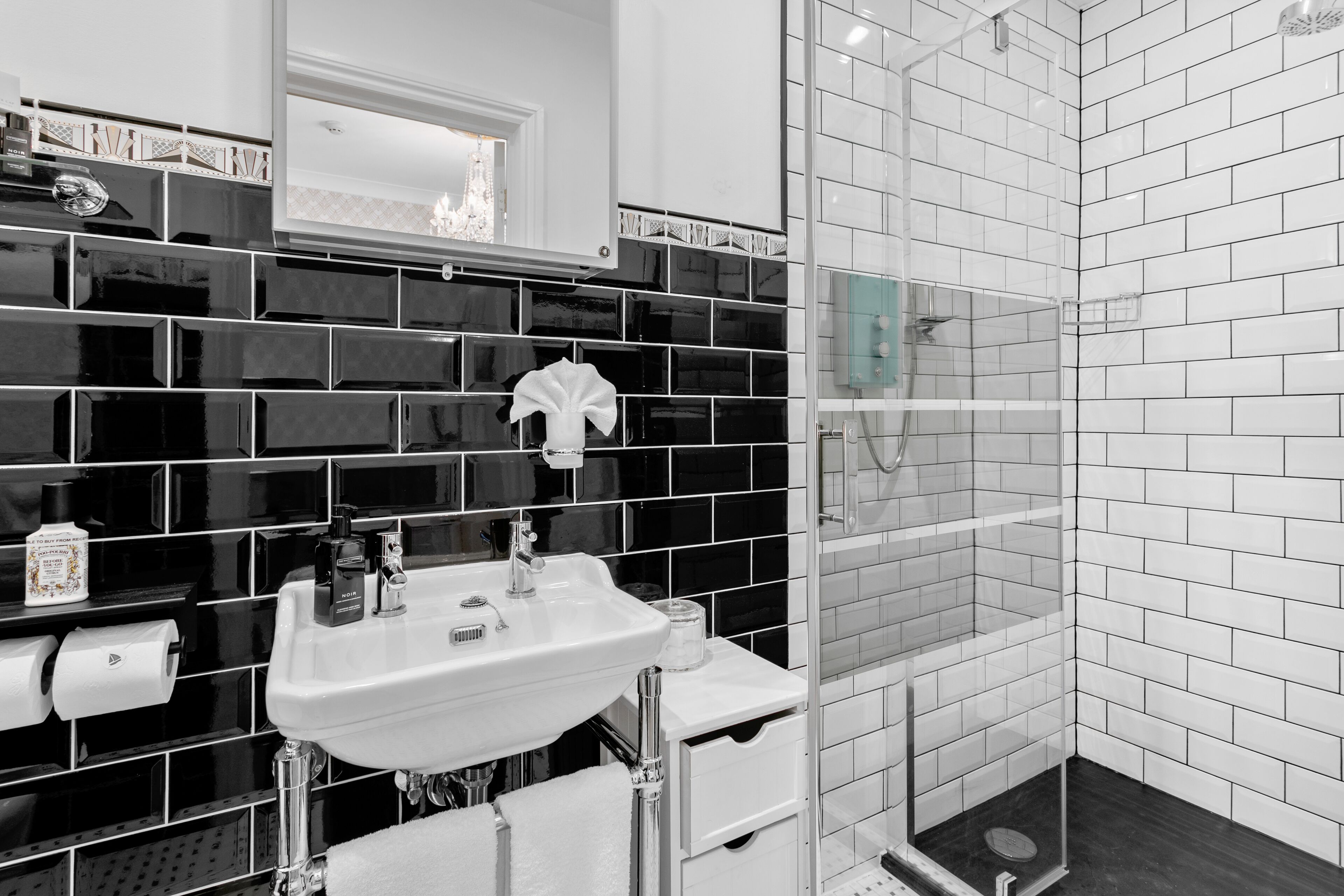 Un baño moderno con un salpicadero de azulejos blanco y negro, un lavabo blanco y una ducha con mampara de vidrio.