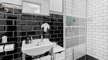 Un baño moderno con un salpicadero de azulejos blanco y negro, un lavabo blanco y una ducha con mampara de vidrio.