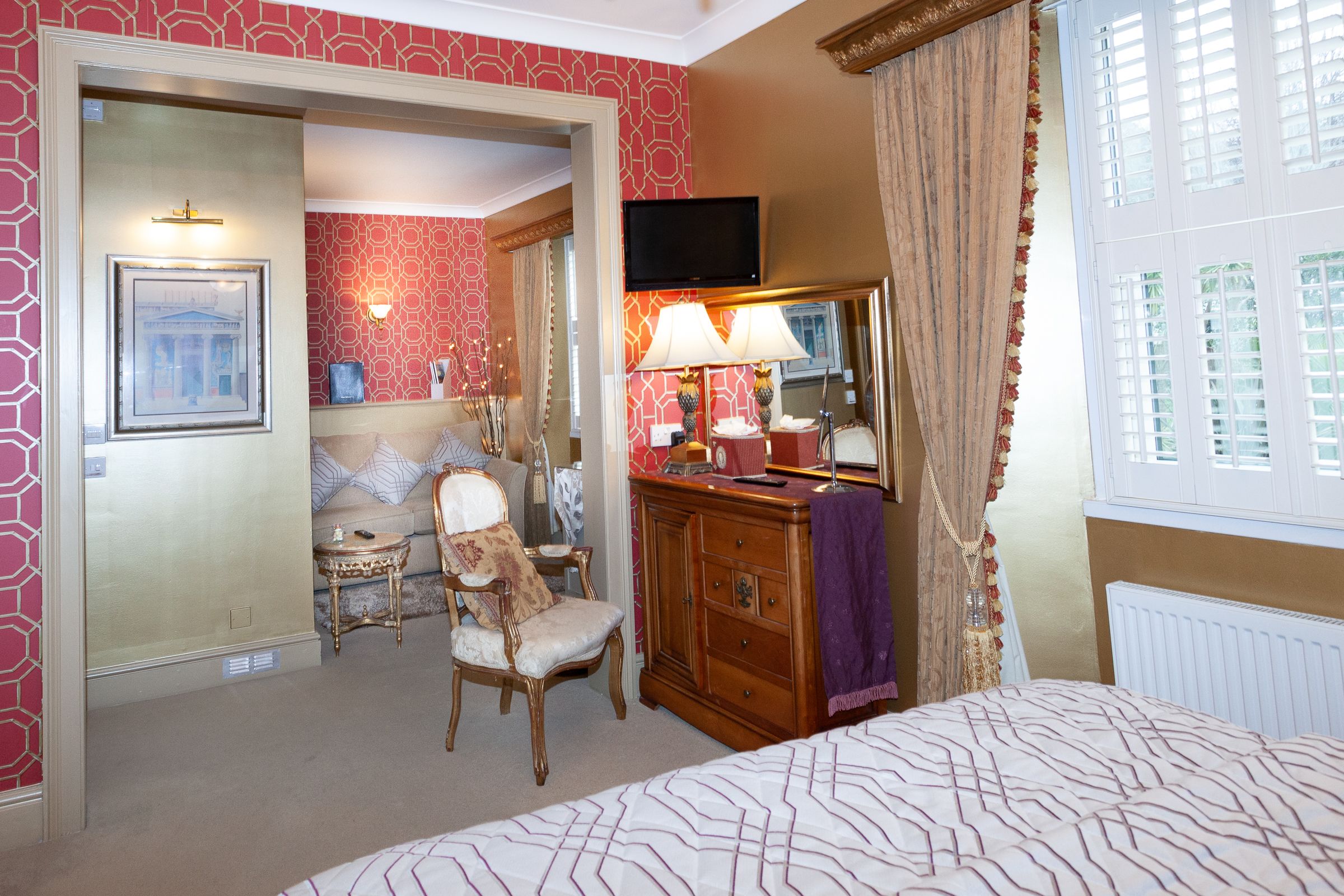 A hotel room with a bed, a vanity with a mirror, a television, a chair, and a small table.