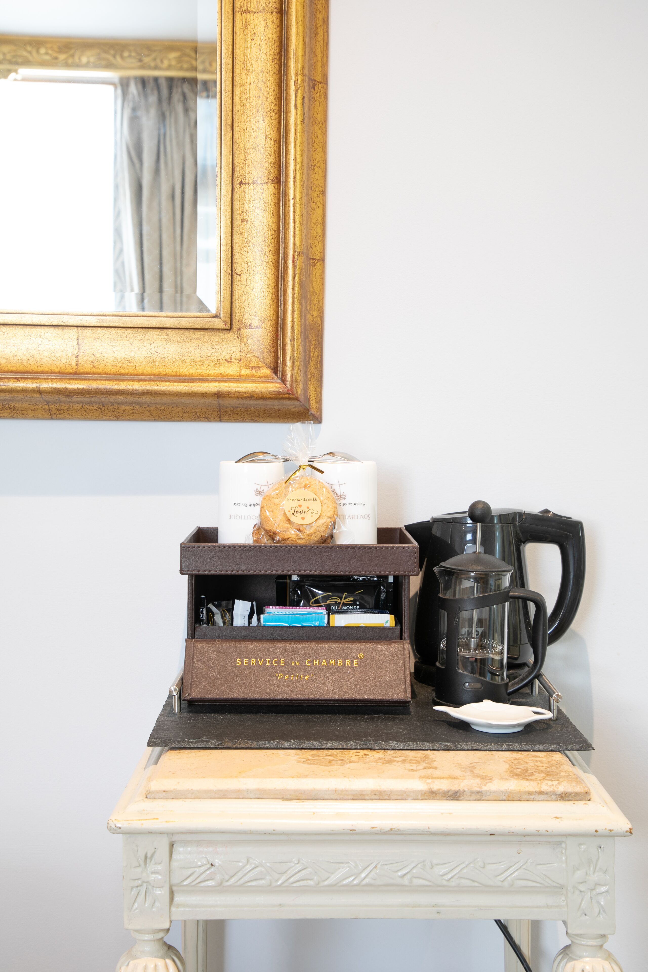 Une petite table avec une machine à café, une boîte étiquetée « SERVICE EN CHAMBRE » et un objet décoratif.