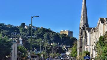 A street with a prominent church spire, a clear blue sky, and a hillside with buildings in the background.
