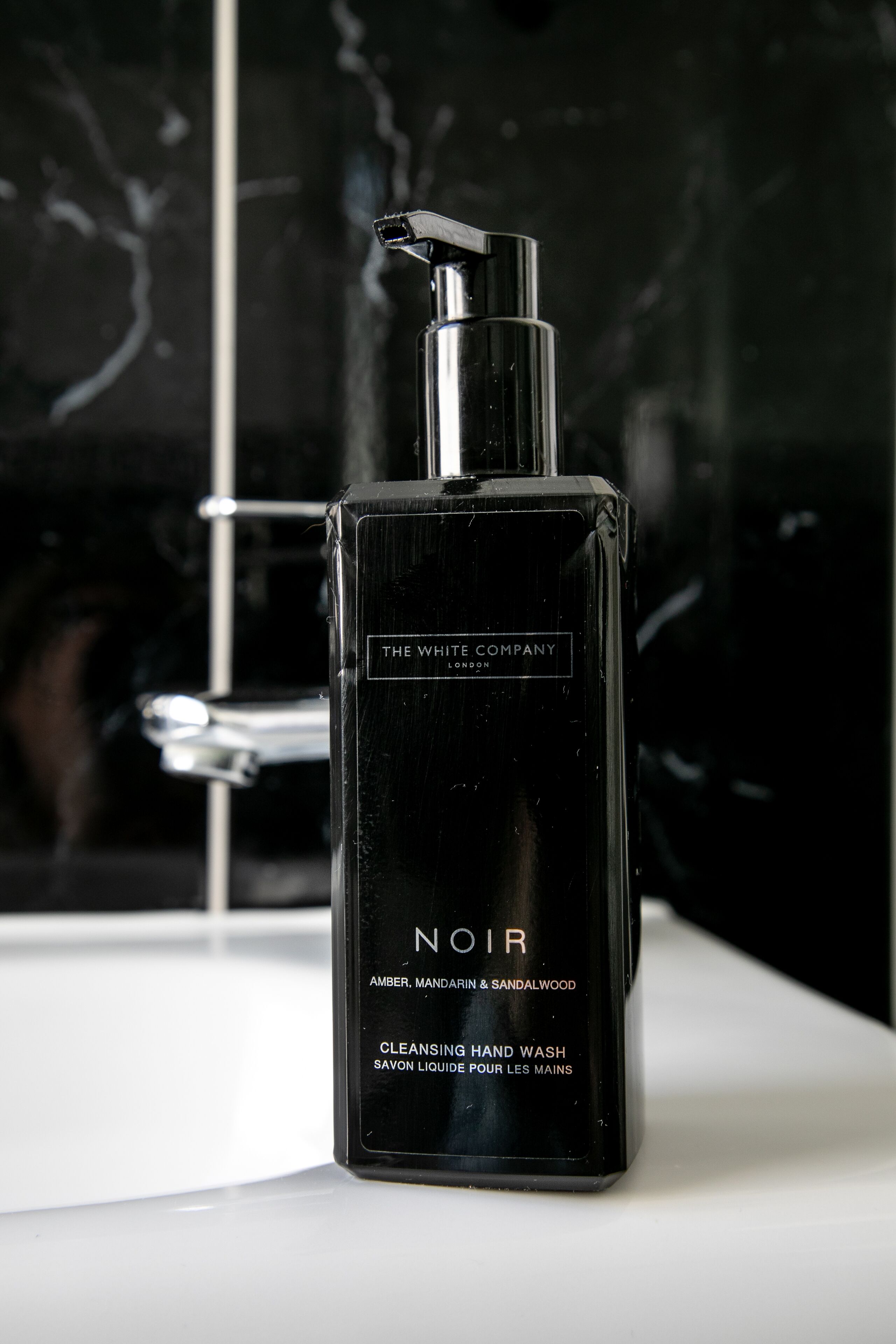 Una botella negra de jabón de manos Noir de The White Company sobre una superficie blanca.