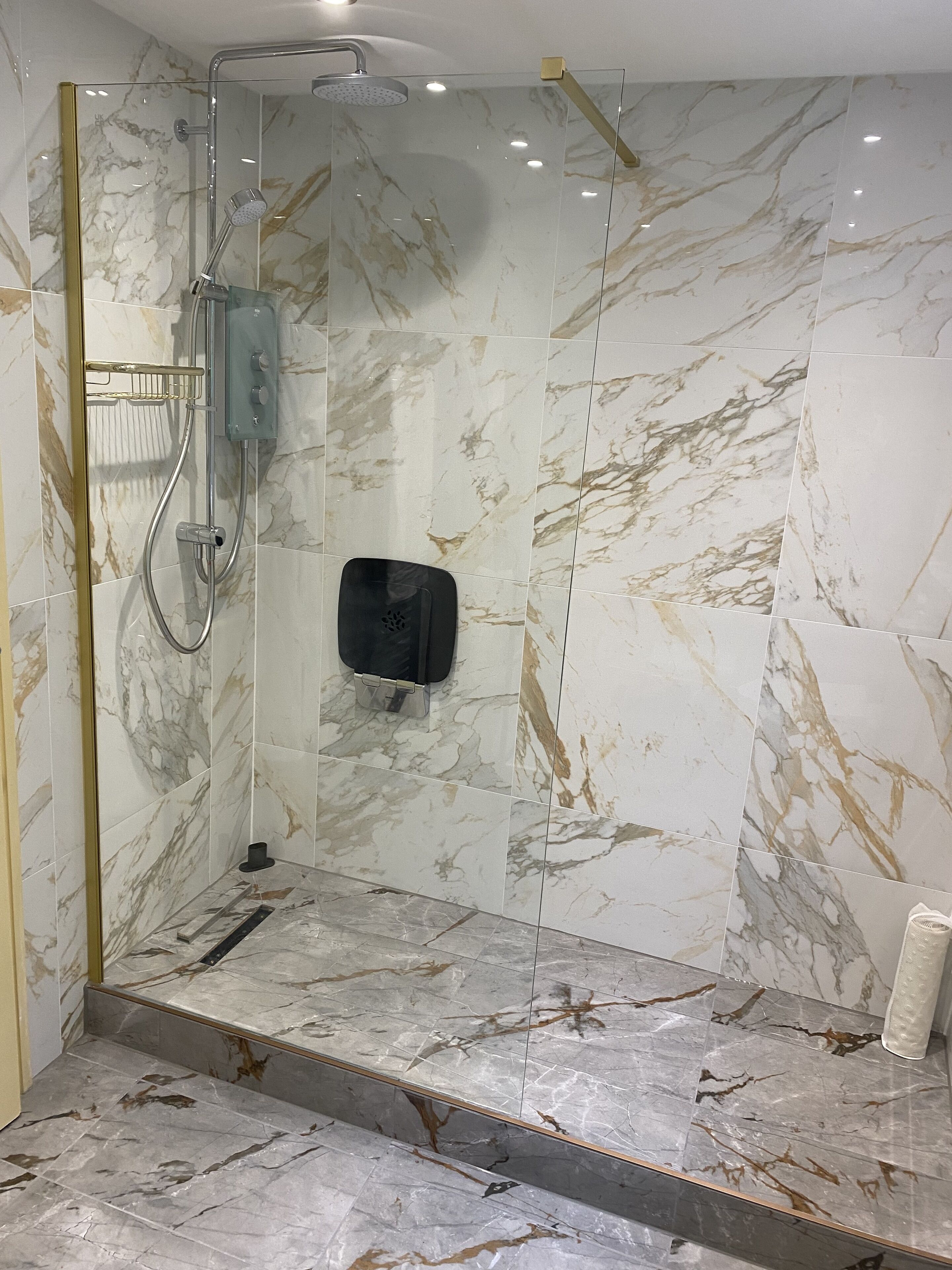A modern shower area with a glass enclosure, marble tiles, and a handheld showerhead.