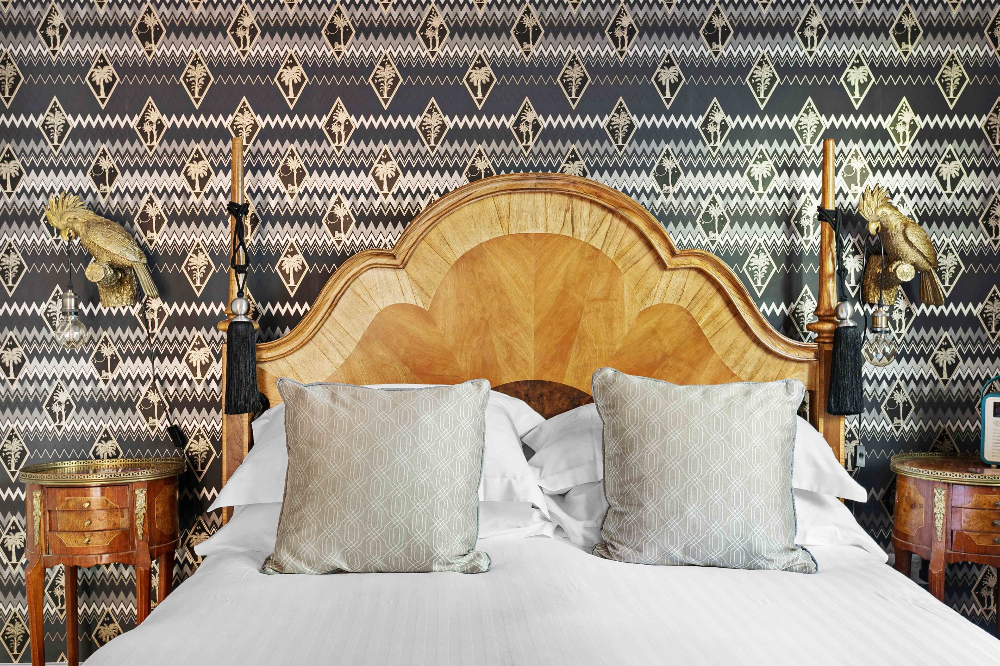Uma cama com cabeceira de madeira, duas almofadas estampadas e parede decorada.