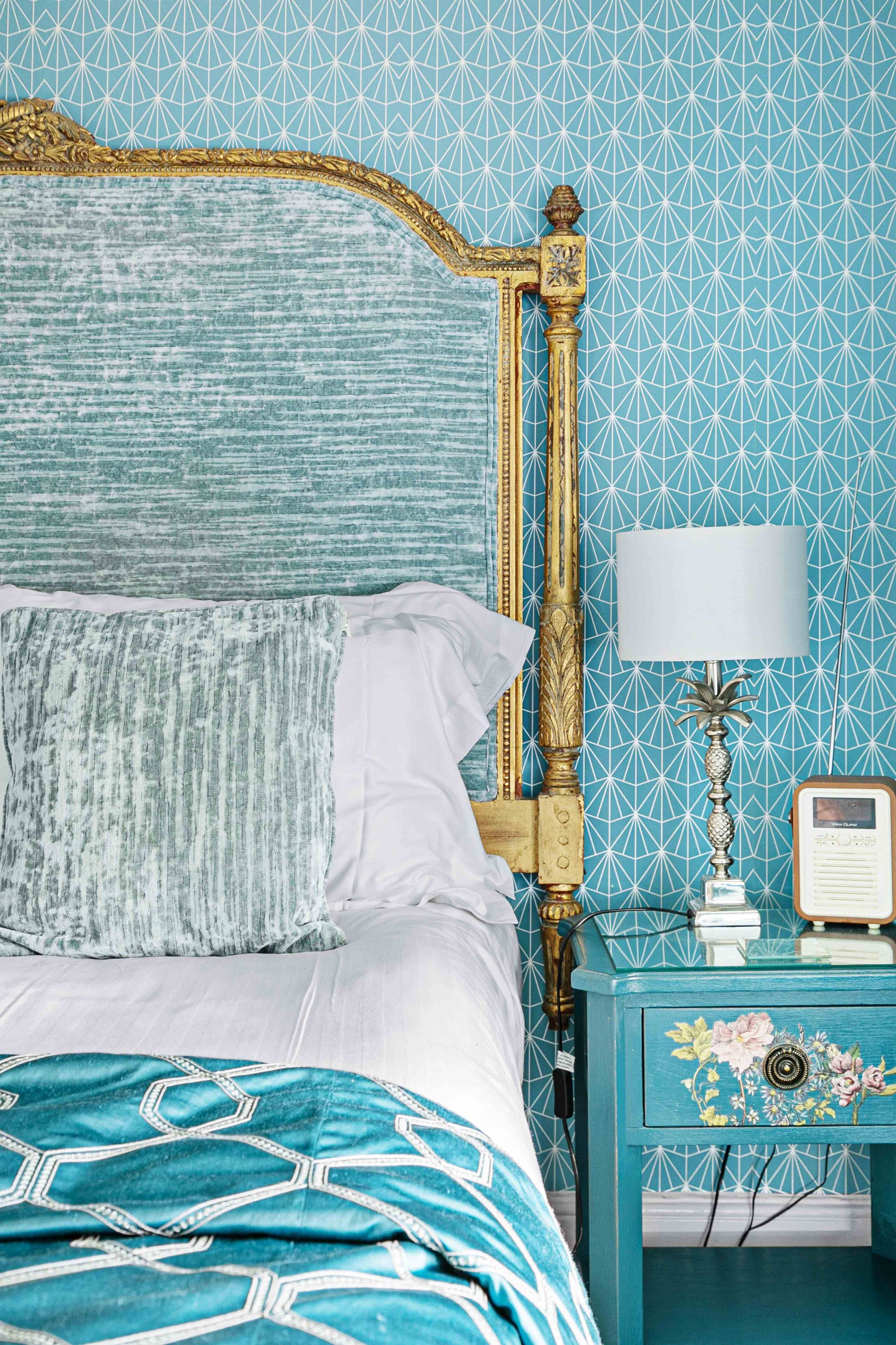 A bed with a patterned headboard, a teal nightstand with a radio, and a floral nightstand.