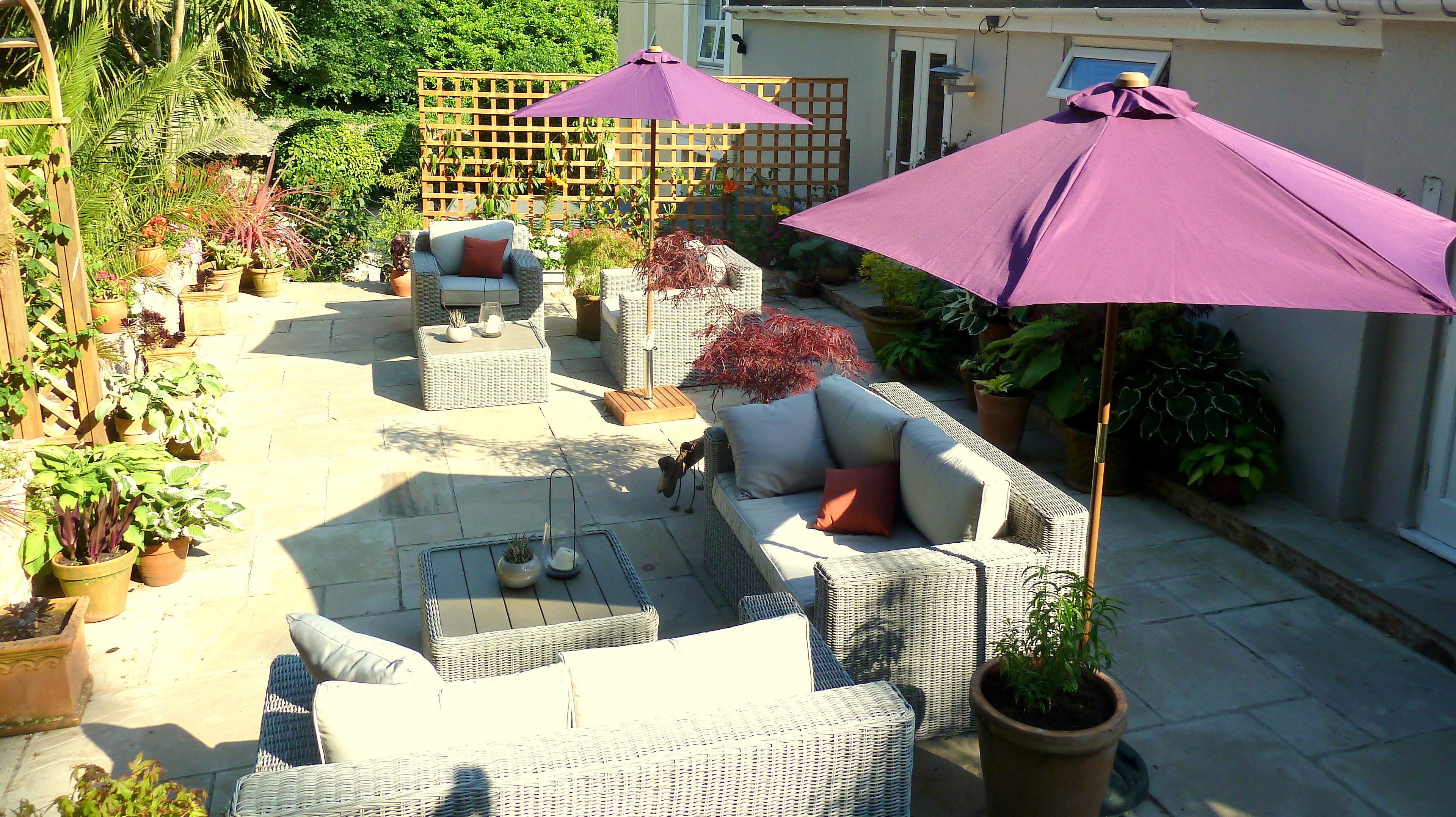 A patio area with wicker furniture, potted plants, and purple umbrellas.