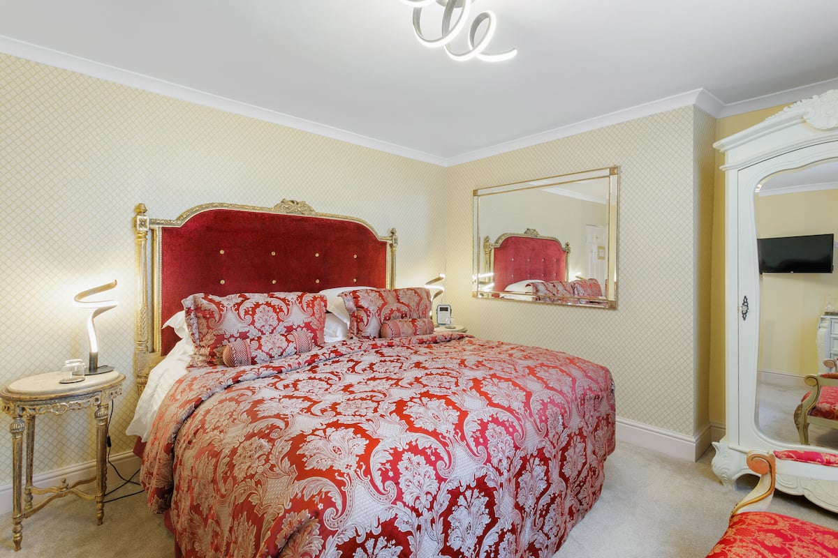 A bedroom with a large bed, a bedside table, a mirror, and a wardrobe.