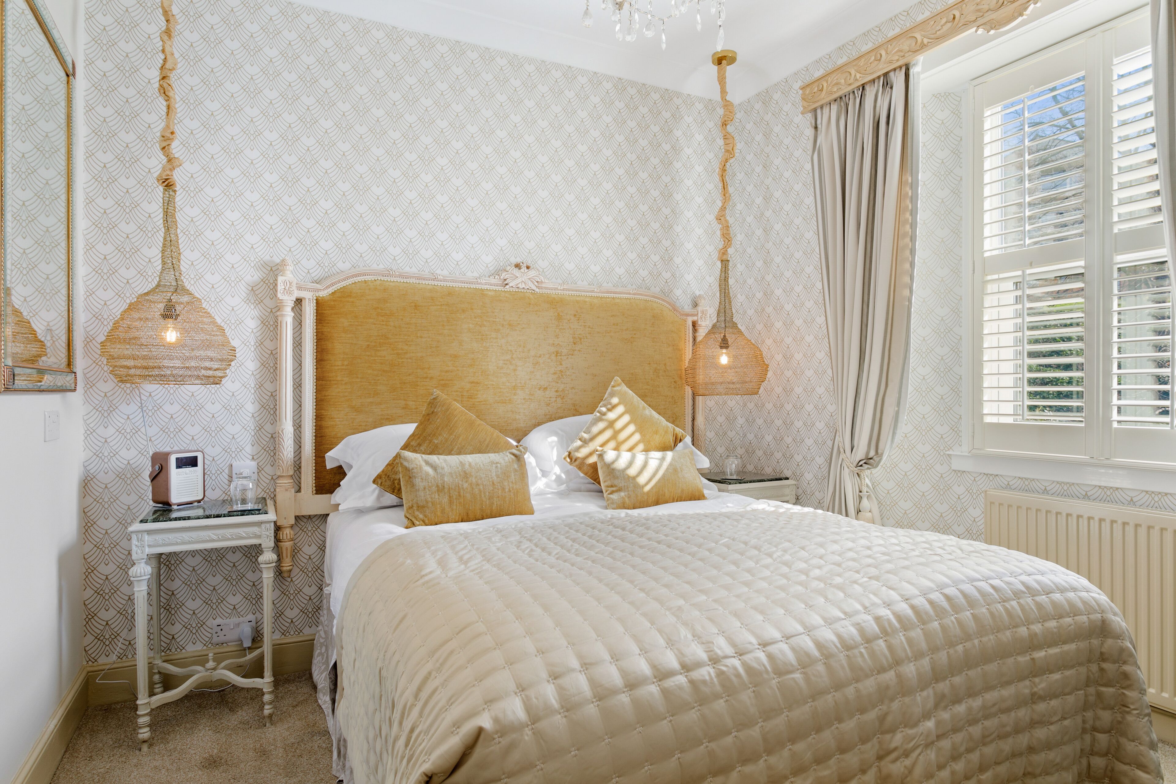 A bedroom with a large bed, a bedside table with a lamp, and a window with curtains.