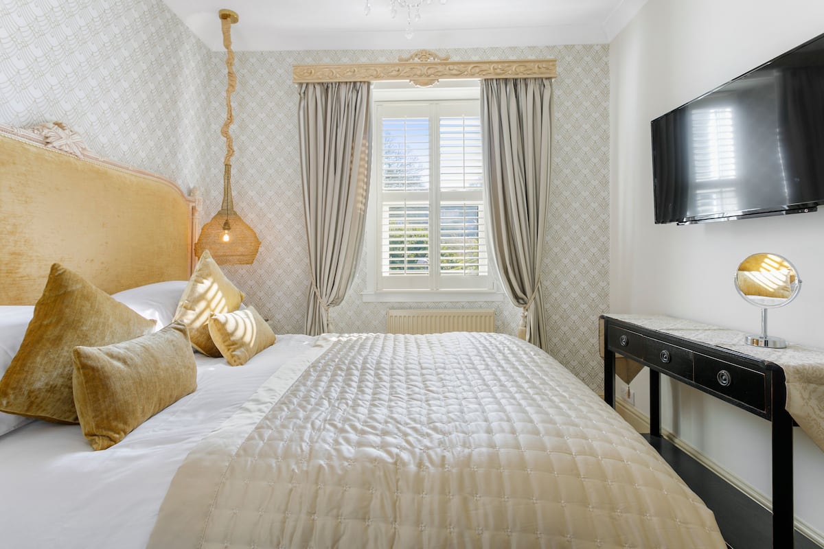 A bedroom with a large bed, a bedside table, a mirror, and a TV mounted on the wall.