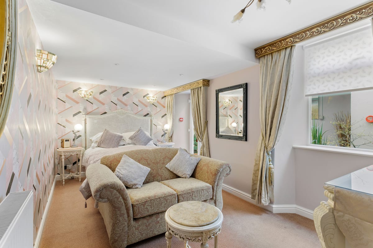 A bedroom with a bed, a sofa, a round table, and a mirror.