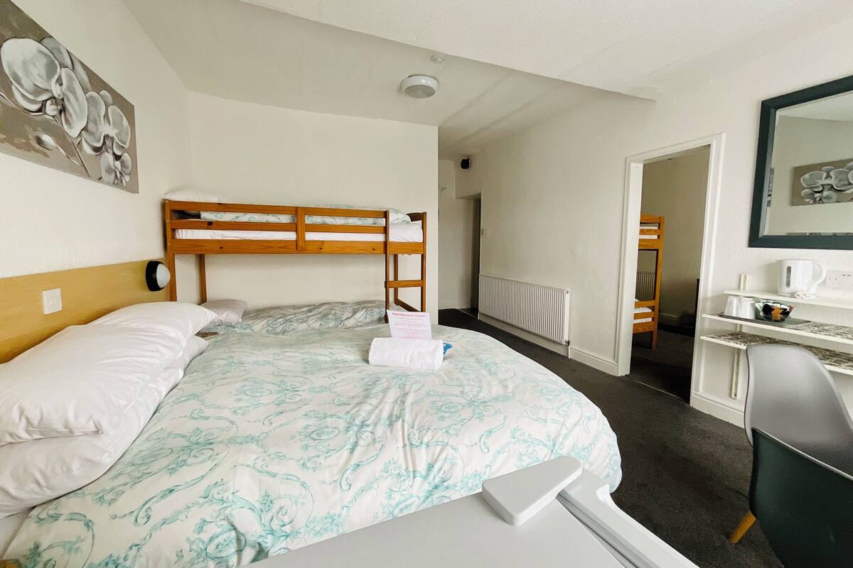 A hotel room with a bunk bed, a desk with a chair, a radiator, and a framed picture on the wall.