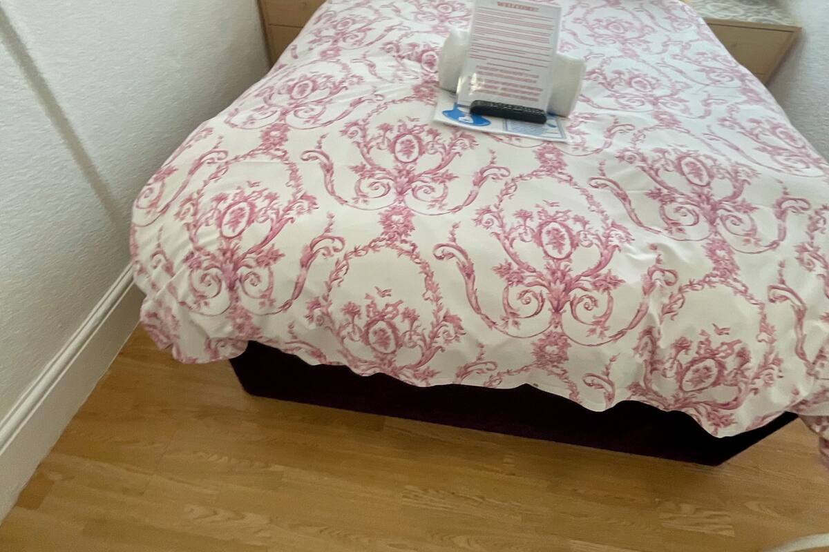 A neatly made bed with a patterned bedspread, a bedside table with a lamp, and a window with curtains.