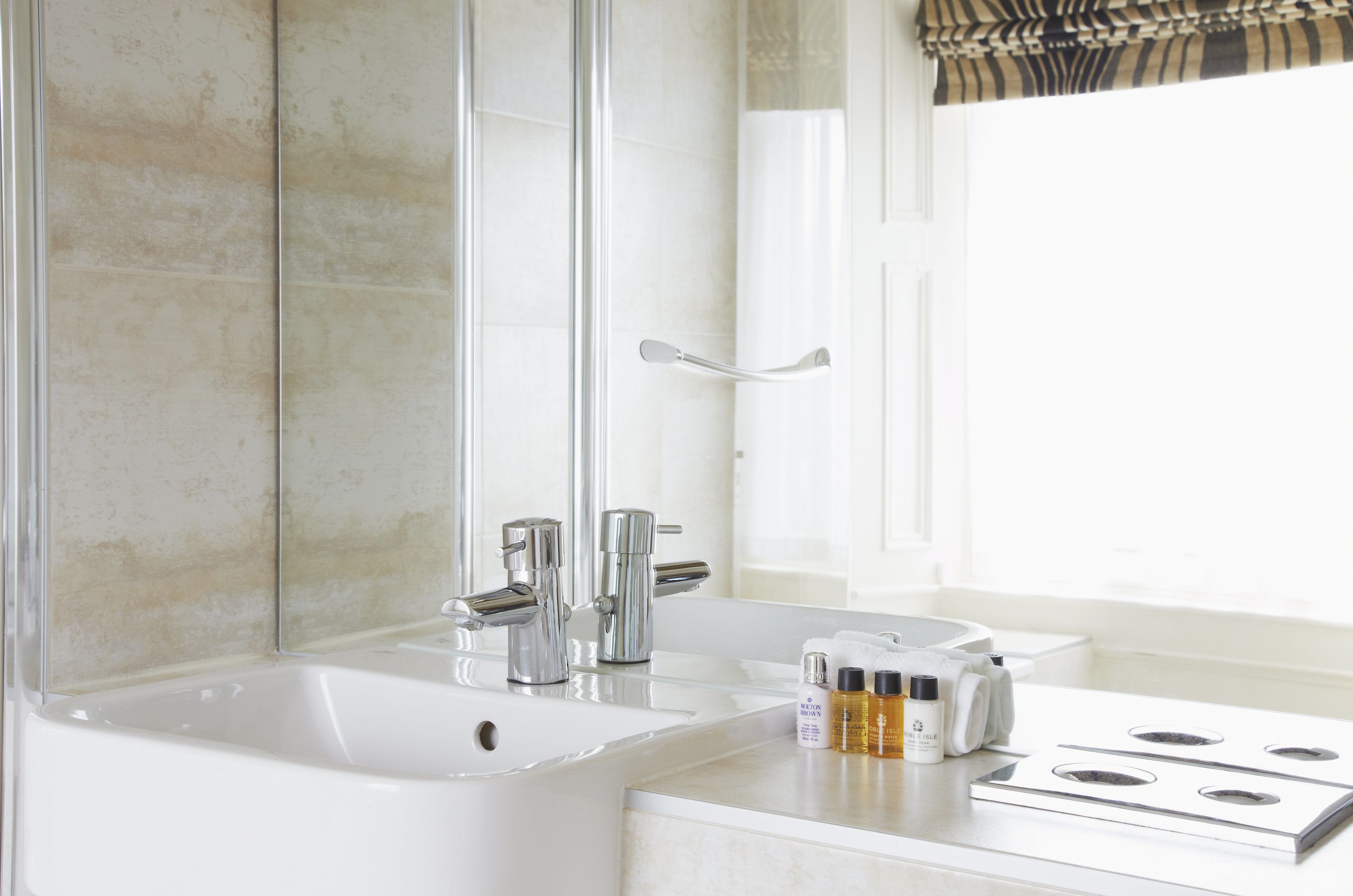 A modern bathroom with a large mirror, a bathtub, a sink, and a window with a striped valance.