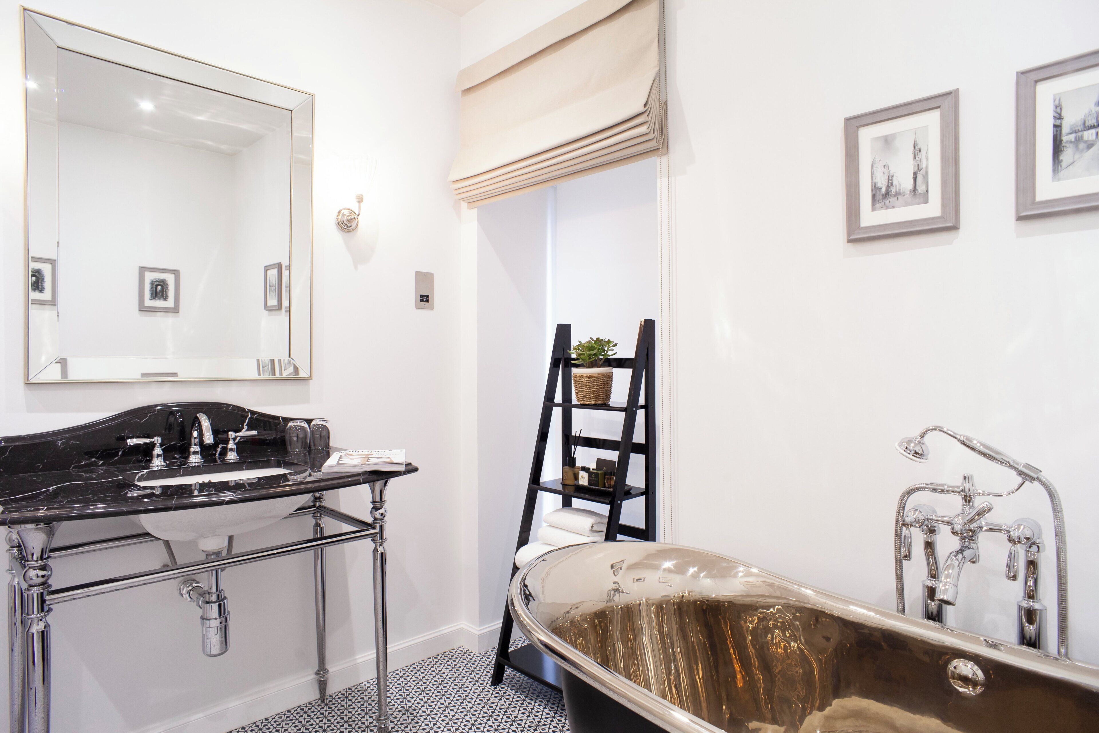 A bathroom with a black bathtub, a large mirror, a sink with a black countertop, and a ladder with a basket.