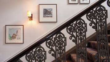 Eine Treppe mit aufwendiger Metallreling, eine Wand mit gerahmten Kunstwerken und eine Wandleuchte.