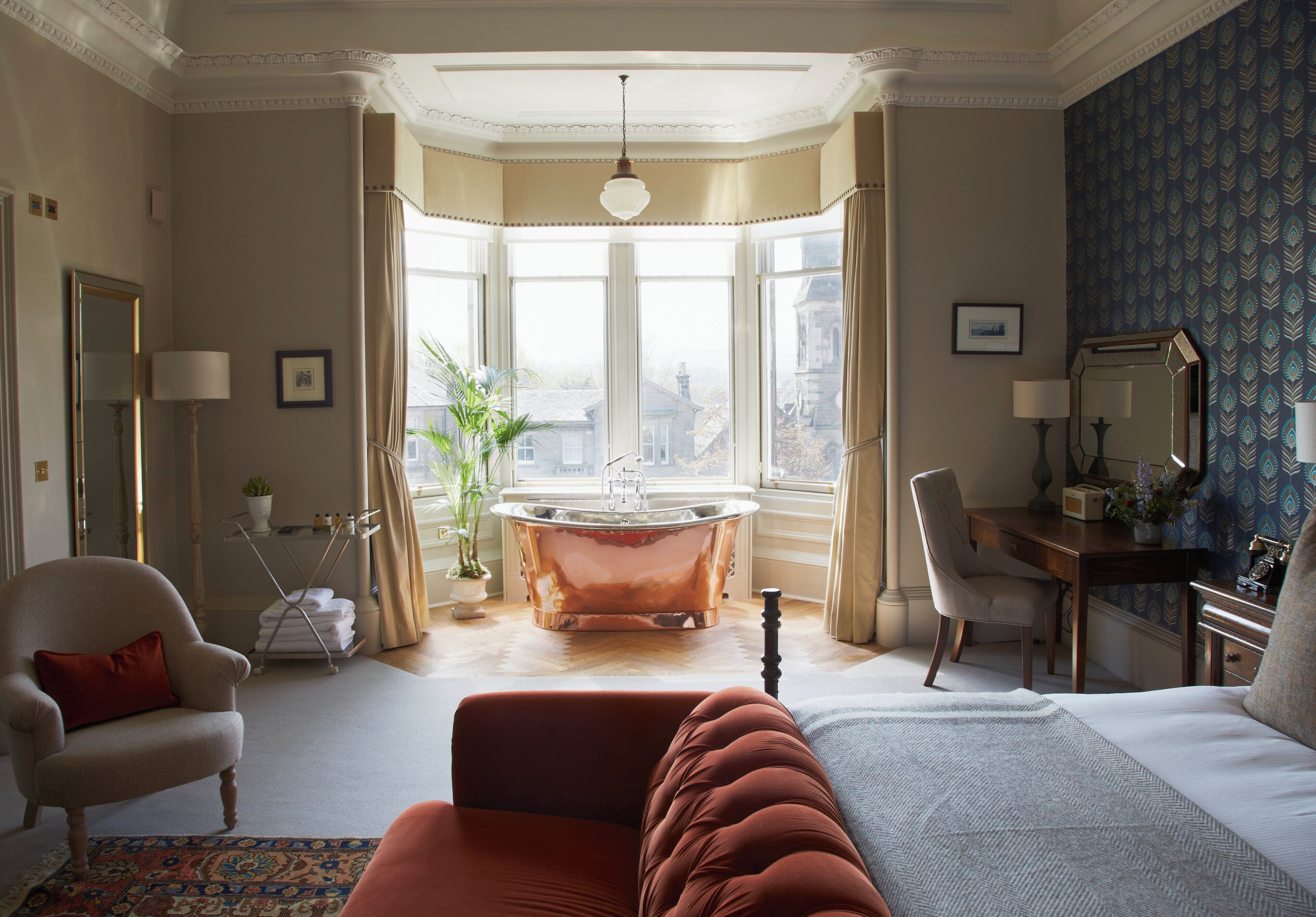 Una habitación con cama, zona de estar con sillón, escritorio, bañera y un gran ventanal con vistas.