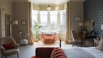 Una habitación con cama, zona de estar con sillón, escritorio, bañera y un gran ventanal con vistas.