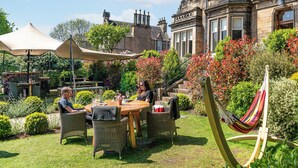 A patio with wicker furniture, a table, and a hammock. - The Roseate Edinburgh (Edinburgh)