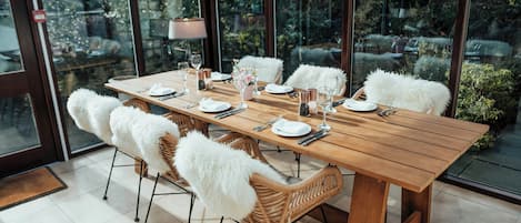 A dining area with a wooden table, white chairs, and a view of a garden through large windows.