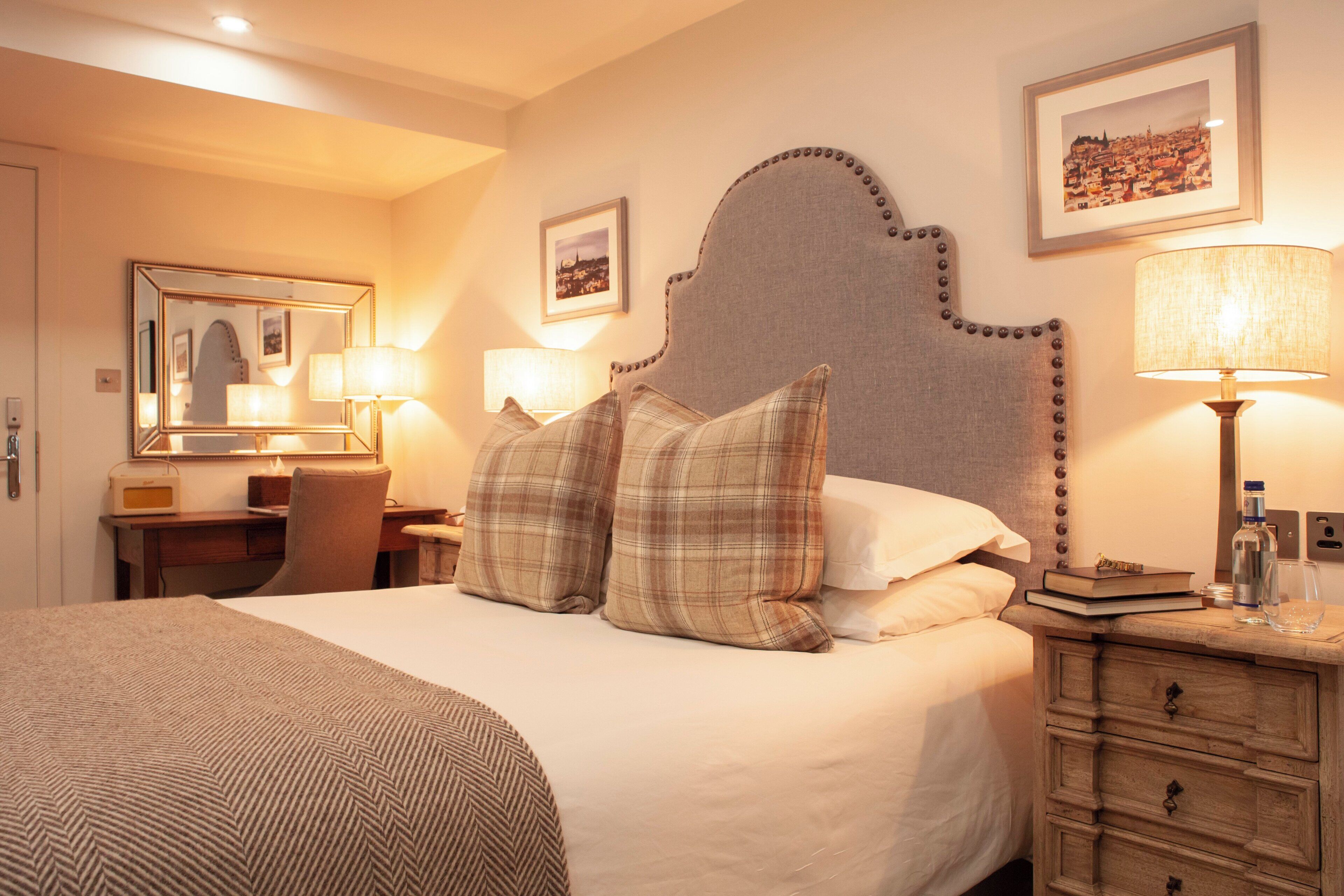 A hotel room with a large bed, a desk with a lamp, a chair, a dresser, and a mirror.