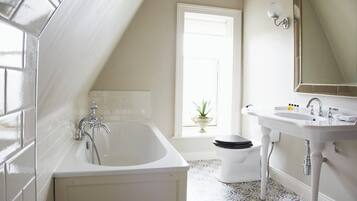 Un baño con bañera, lavabo e inodoro. Hay una ventana con una planta en el alféizar.