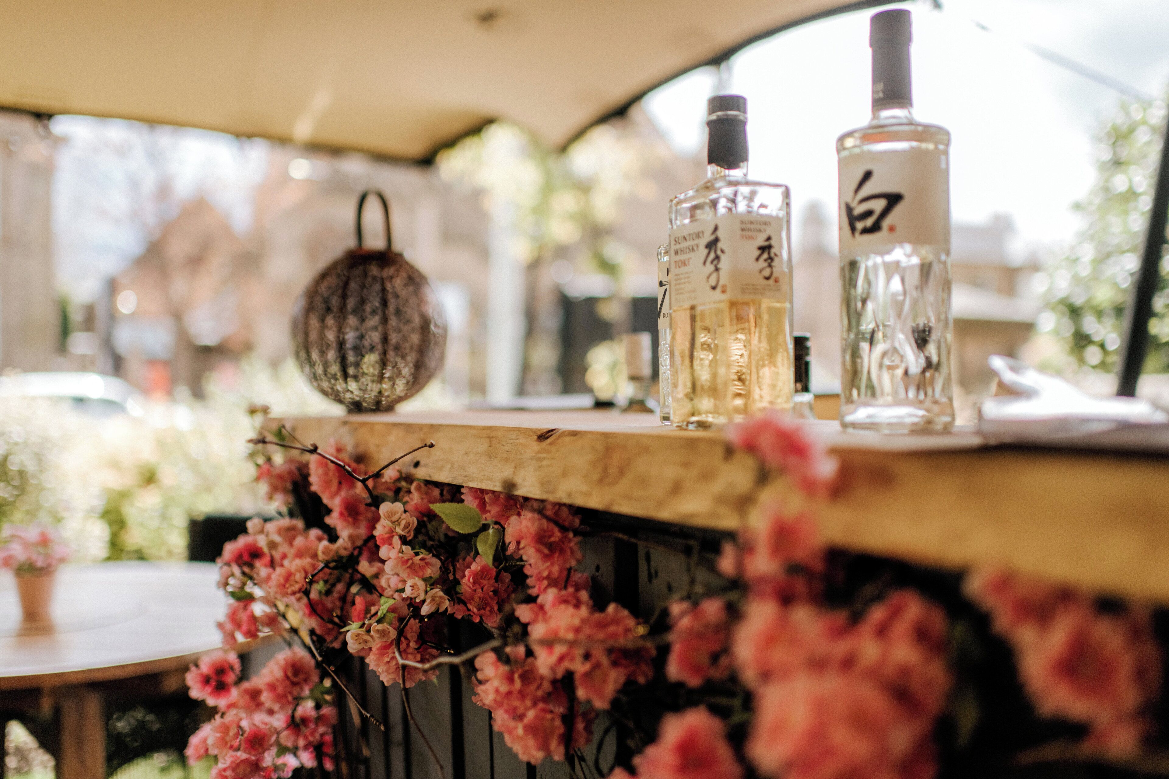 A table with bottles and a hanging bag, surrounded by pink flowers.