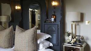 A bedroom with a bed, pillows, a nightstand, a lamp, a mirror, and a bottle of wine. - The Roseate Edinburgh (Edinburgh)