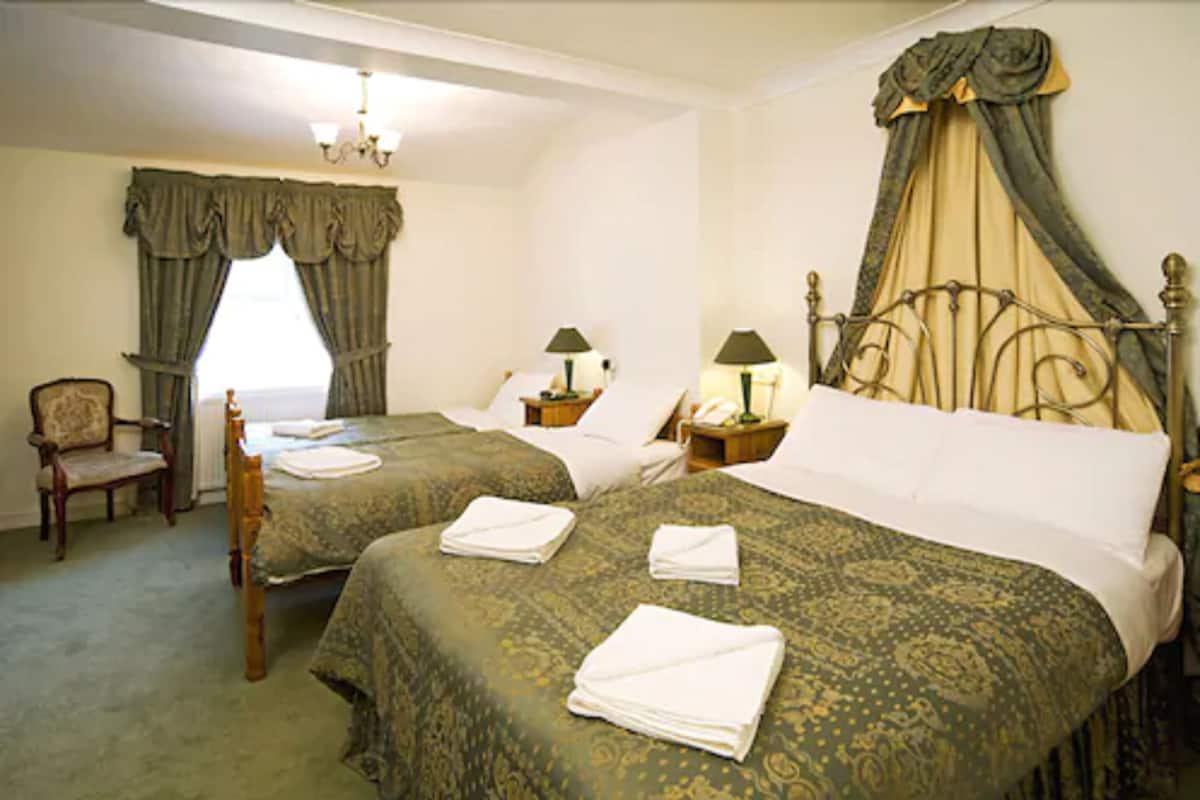 A hotel room with two beds, a chair, a nightstand with a lamp, and a window with curtains.